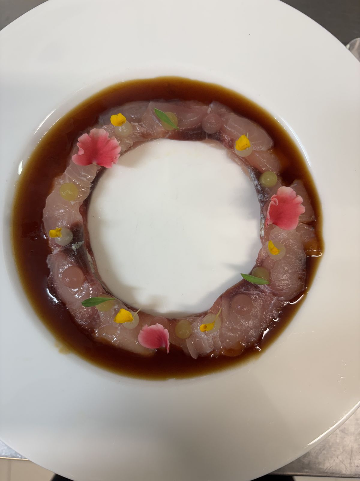 Ricciola agli agrumi disposta ad anello in una salsa ponzu, con petali e fiori