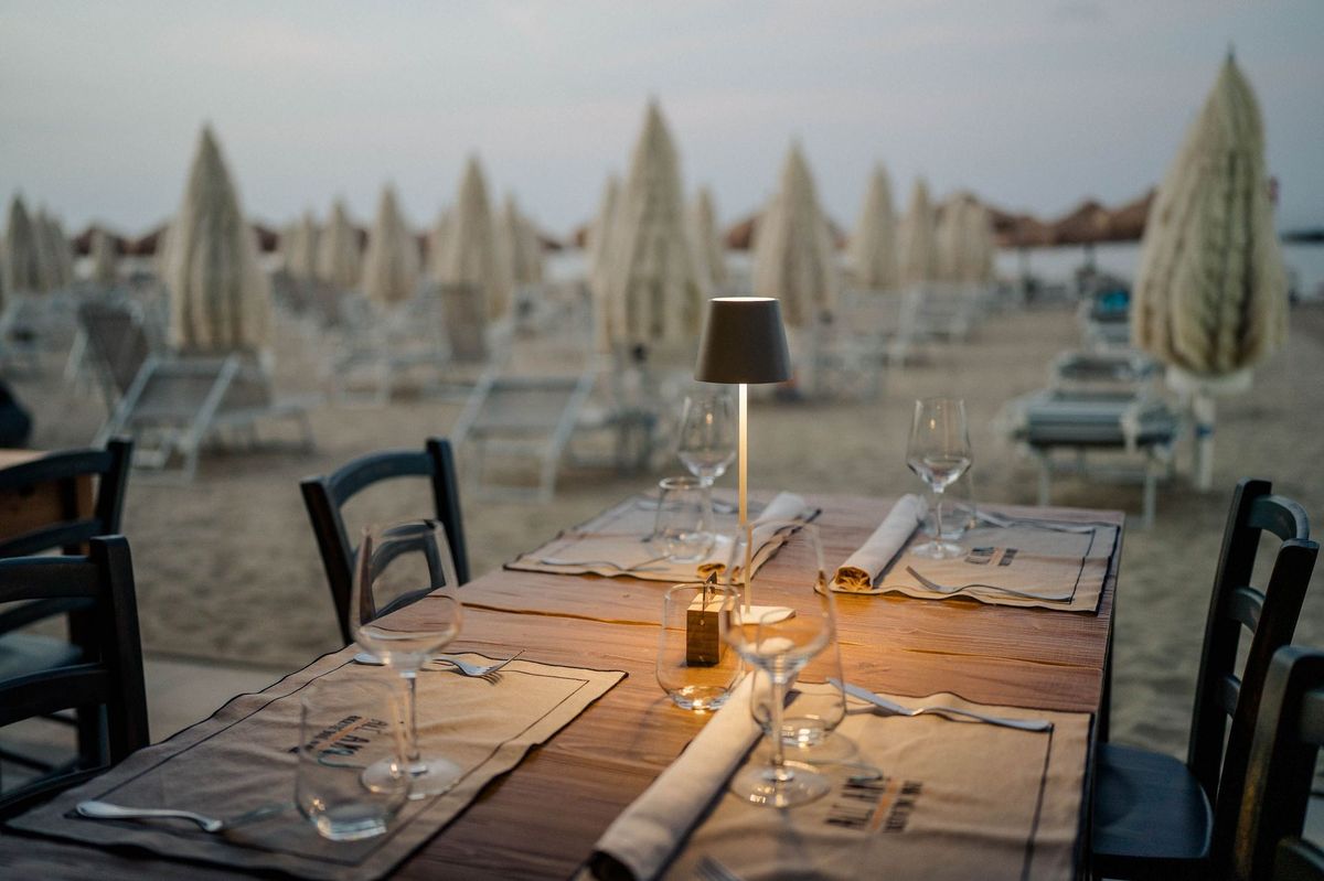 Tavolo apparecchiato al tramonto sulla spiaggia di All'Amo, con la lampada accesa e gli ombrelloni chiusi